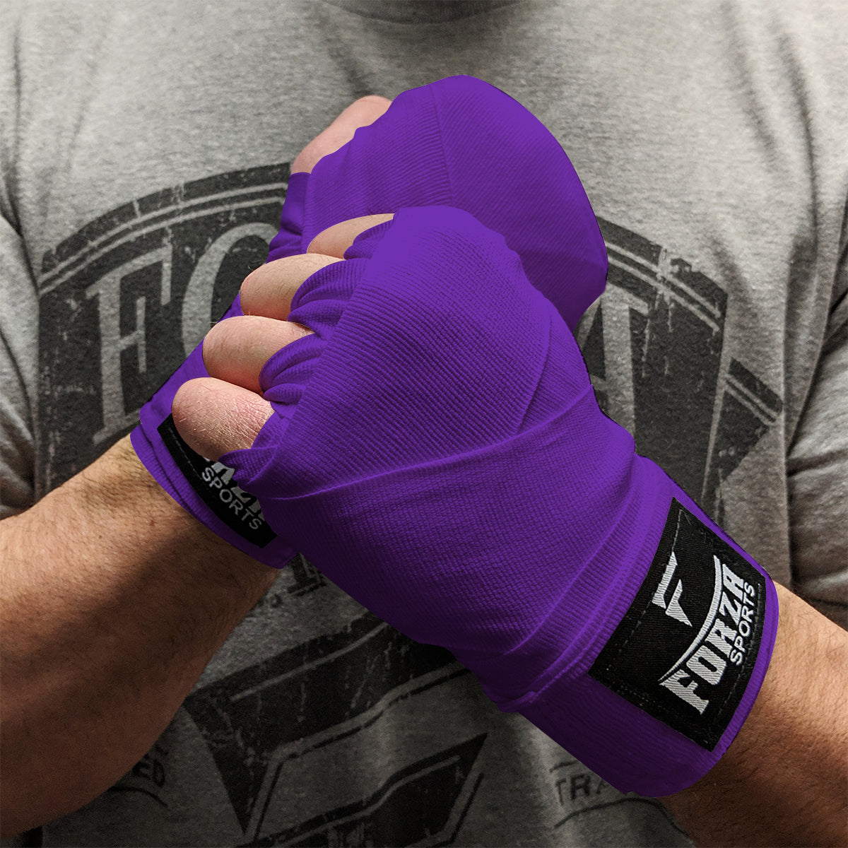 Person wearing purple boxing hand wraps with Forza Sports logo, against a gray t-shirt background.