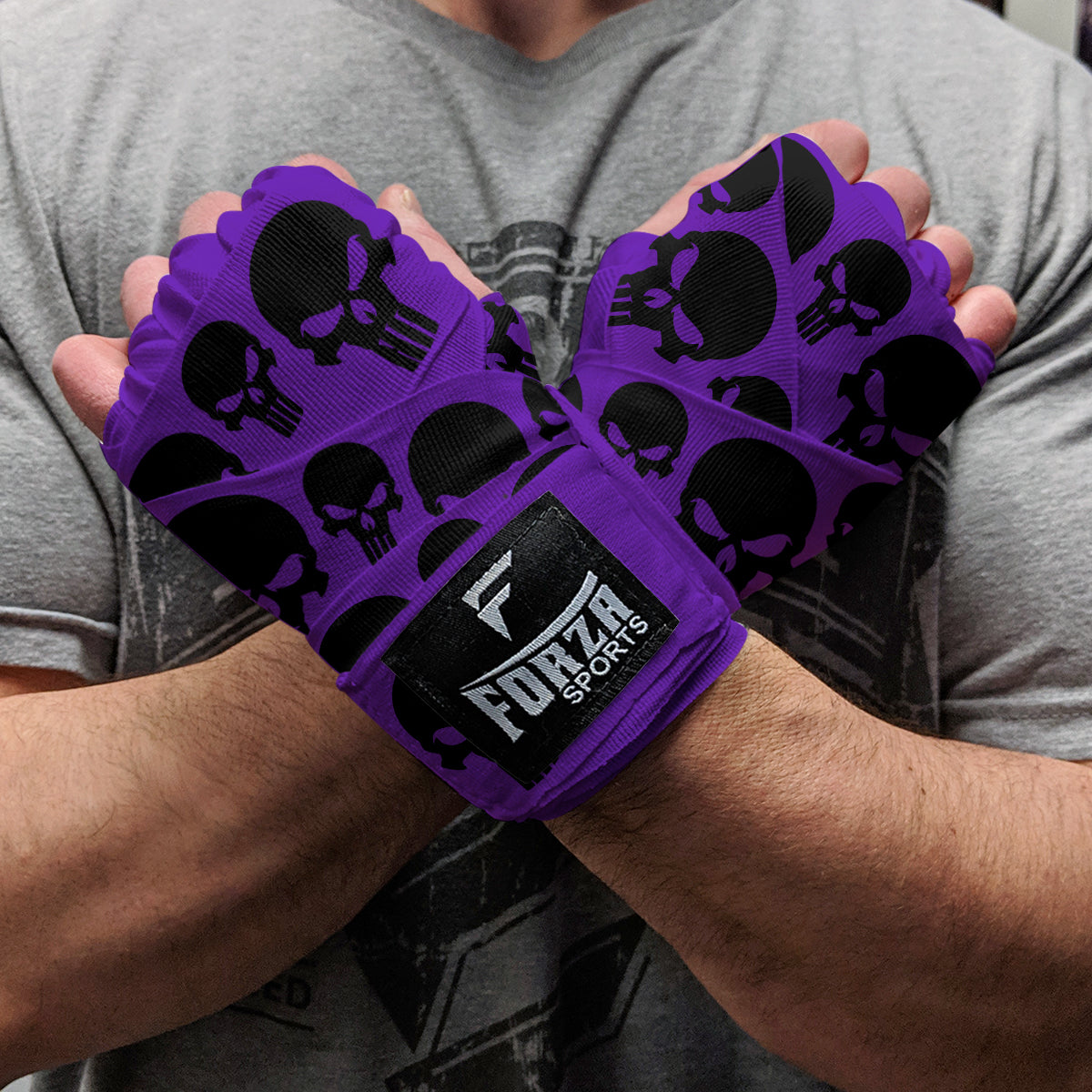 Purple wrist wraps with black skull patterns held by a person wearing a gray shirt.