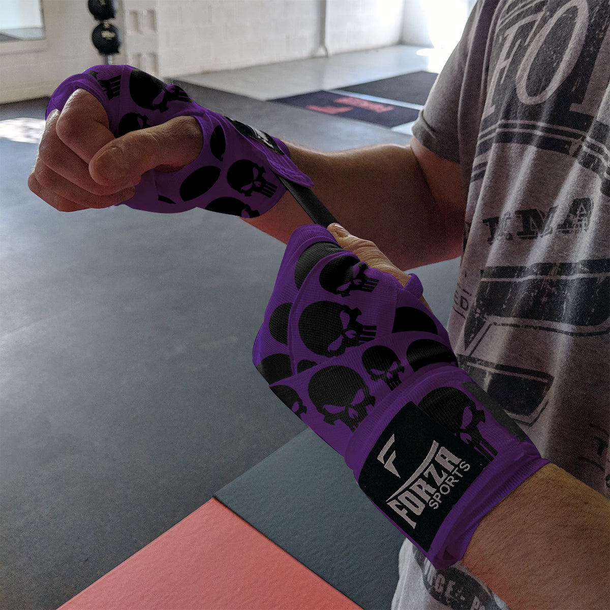 Person wearing purple boxing gloves with black skull patterns in a gym setting