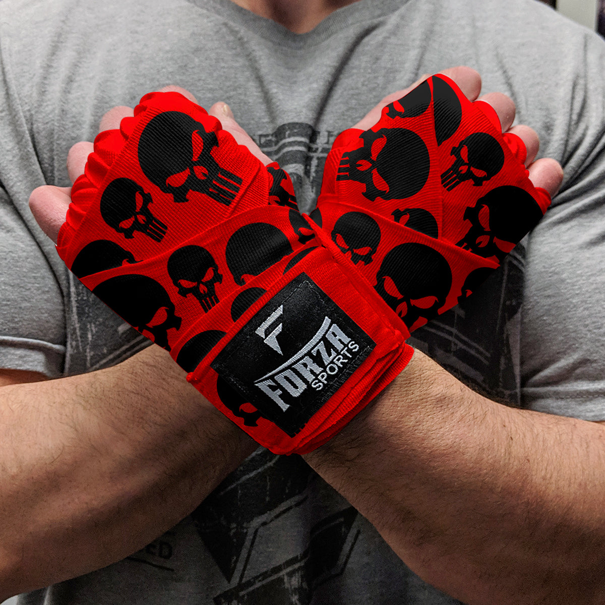 Red boxing gloves with black skull patterns held by a person wearing a gray shirt.