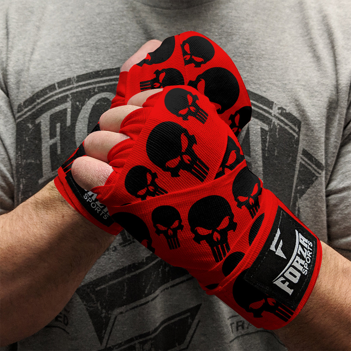 Red boxing hand wraps with black skull designs worn by a person, against a gray t-shirt background.