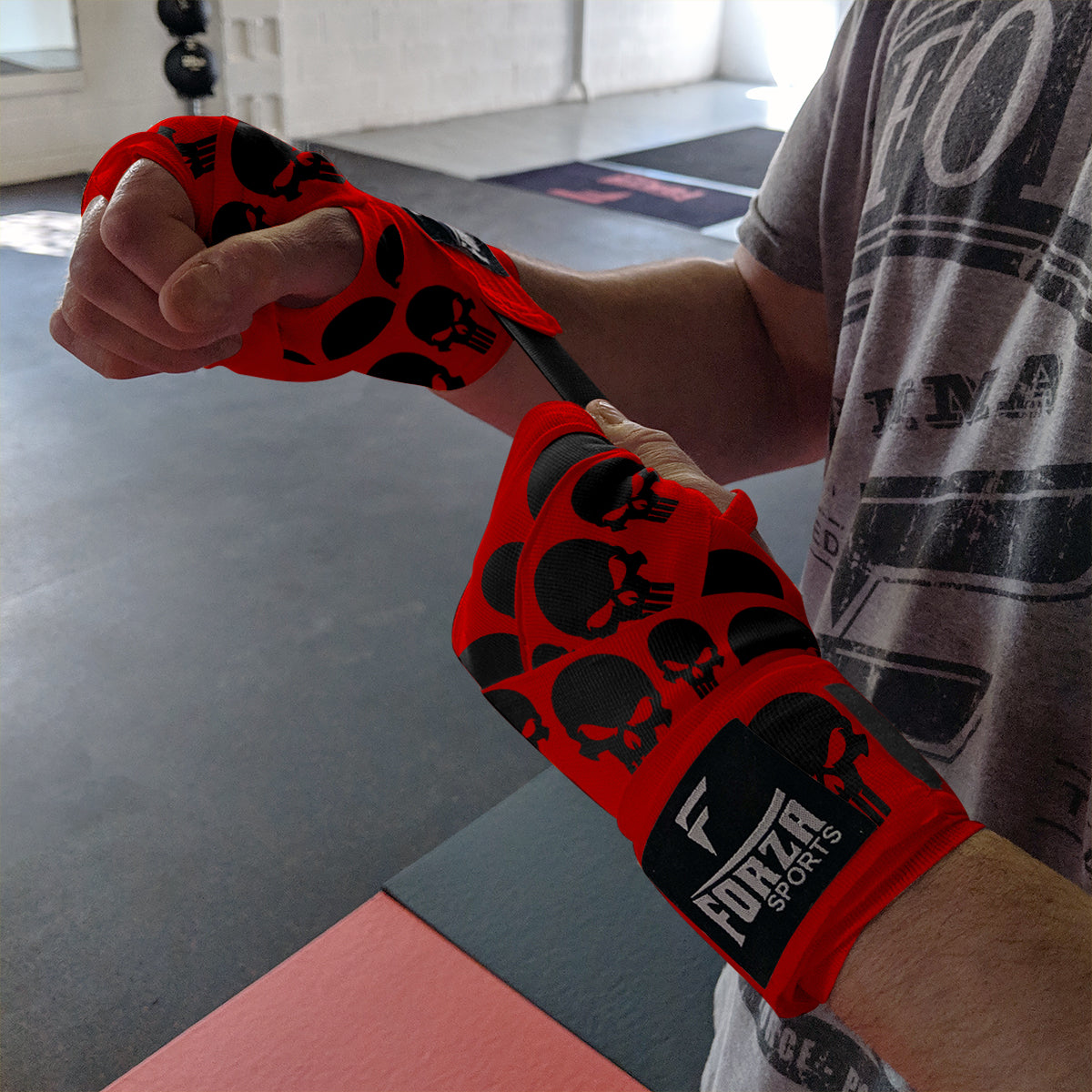Person wearing red and black boxing wraps with a visible brand logo in a gym setting.