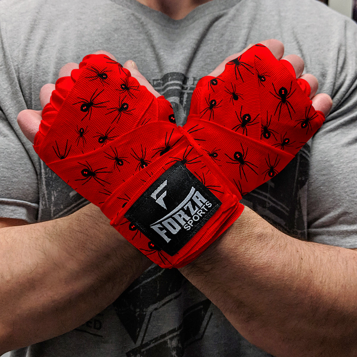 Red wrist wraps with black spider pattern held by a person, branded 'Forza Sports'.