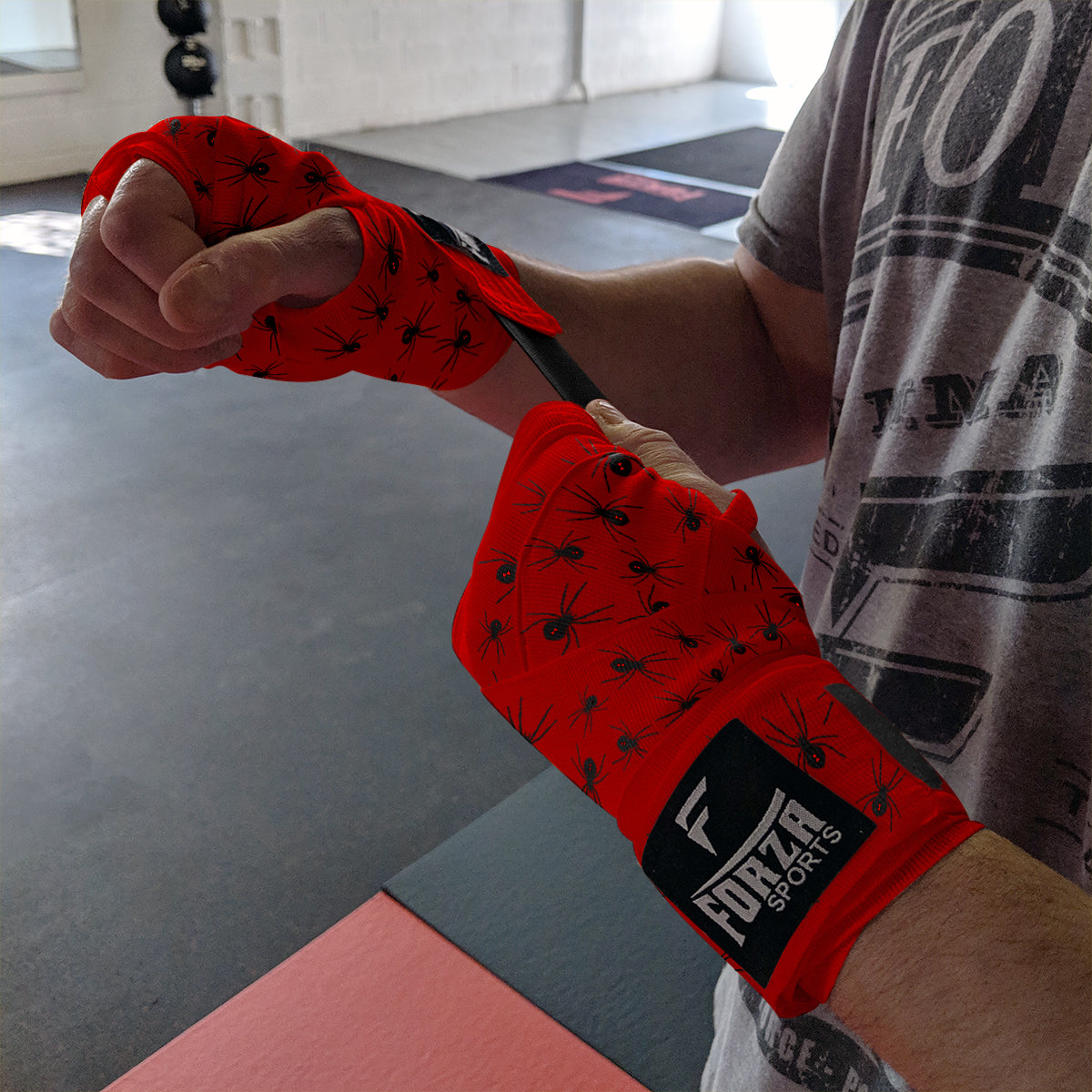 Person wrapping their wrist with red boxing wraps featuring a brand logo in a gym setting.
