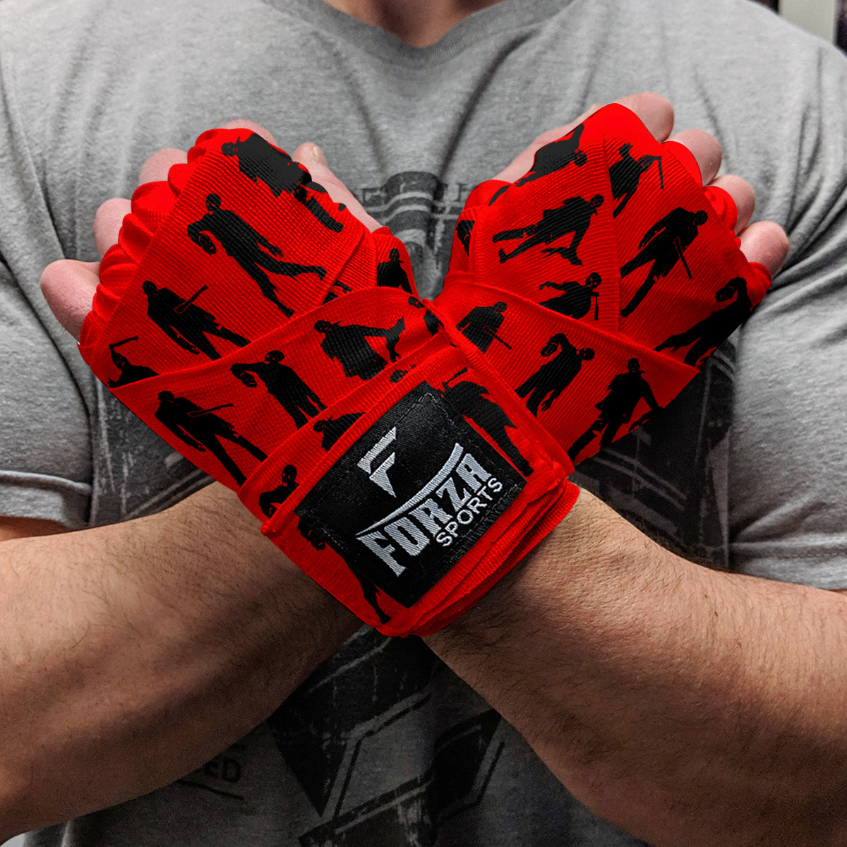 Red boxing hand wraps with black silhouettes and Forza Sports logo held by a person wearing a gray shirt.