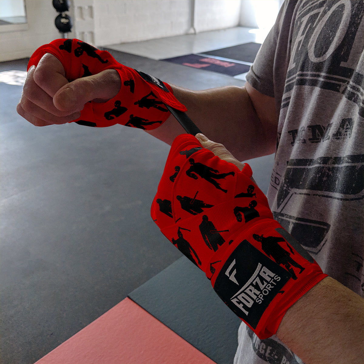 Person wearing red boxing wraps with black silhouettes and 'Forza Sports' branding in a gym setting.