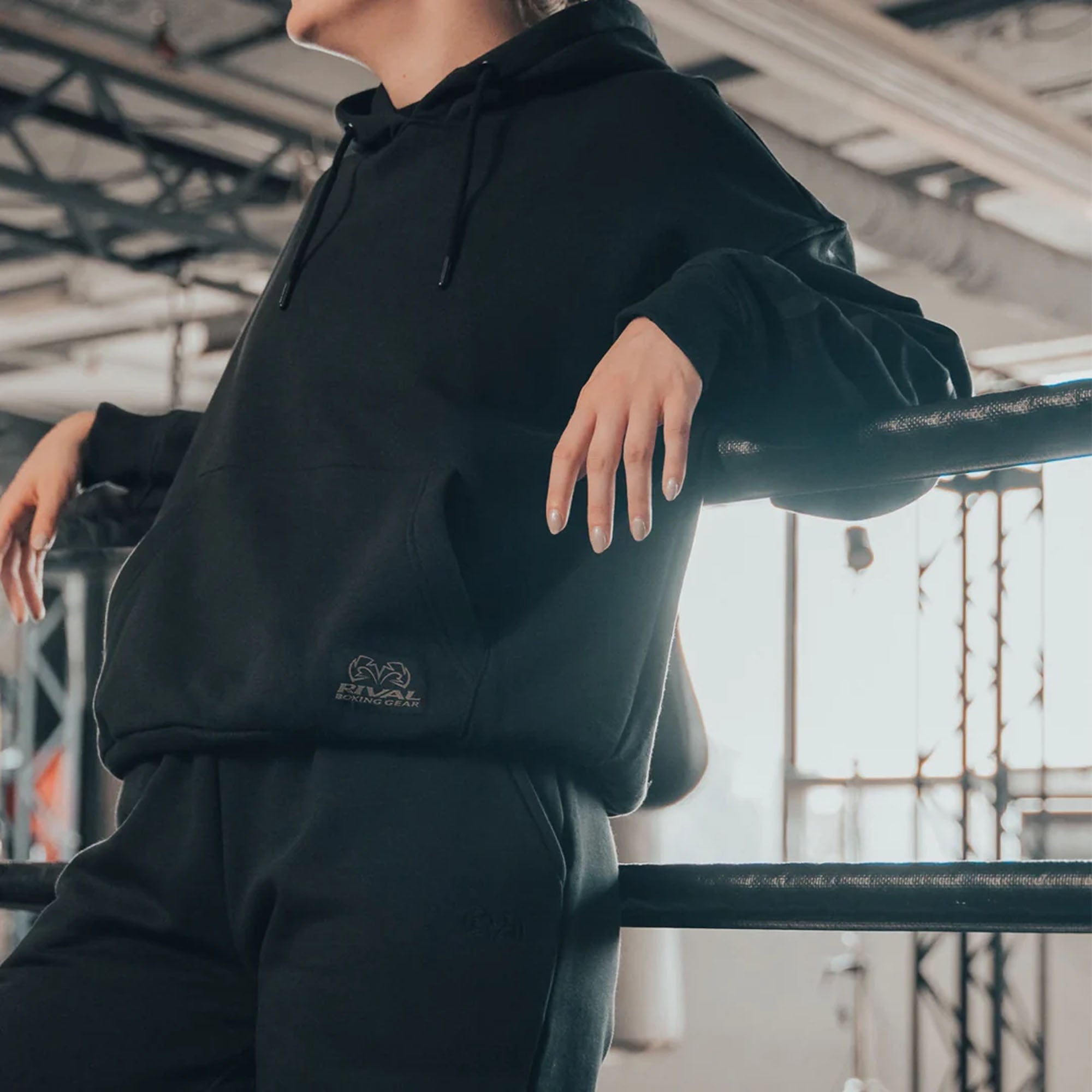 Person wearing a black heavyweight fleece hoodie with a logo, standing indoors.