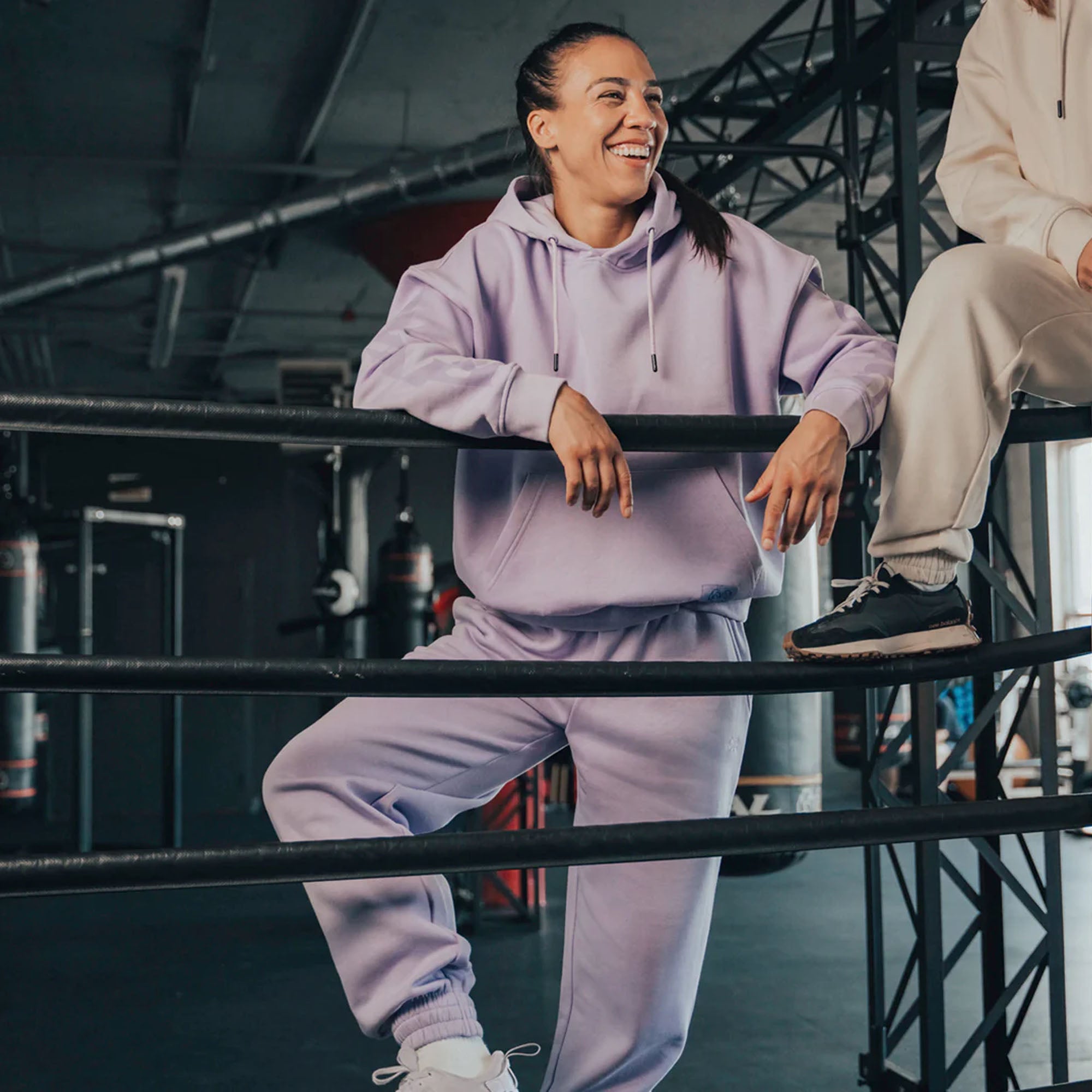 Person wearing a purple heavyweight fleece hoodie tracksuit sitting on a metal railing indoors.