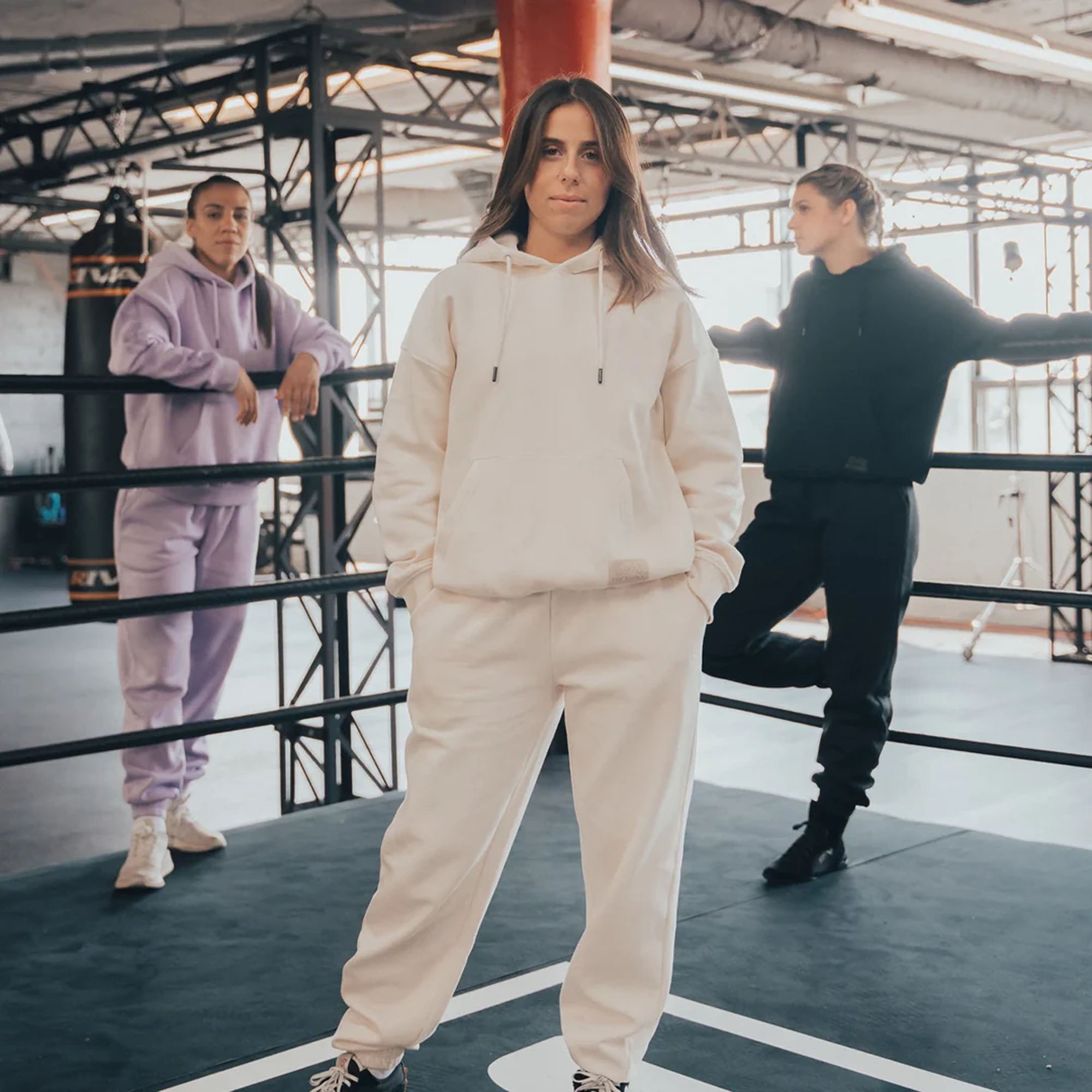 Person wearing a beige heavyweight fleece hoodie tracksuit standing in a boxing ring with two other people in the background.