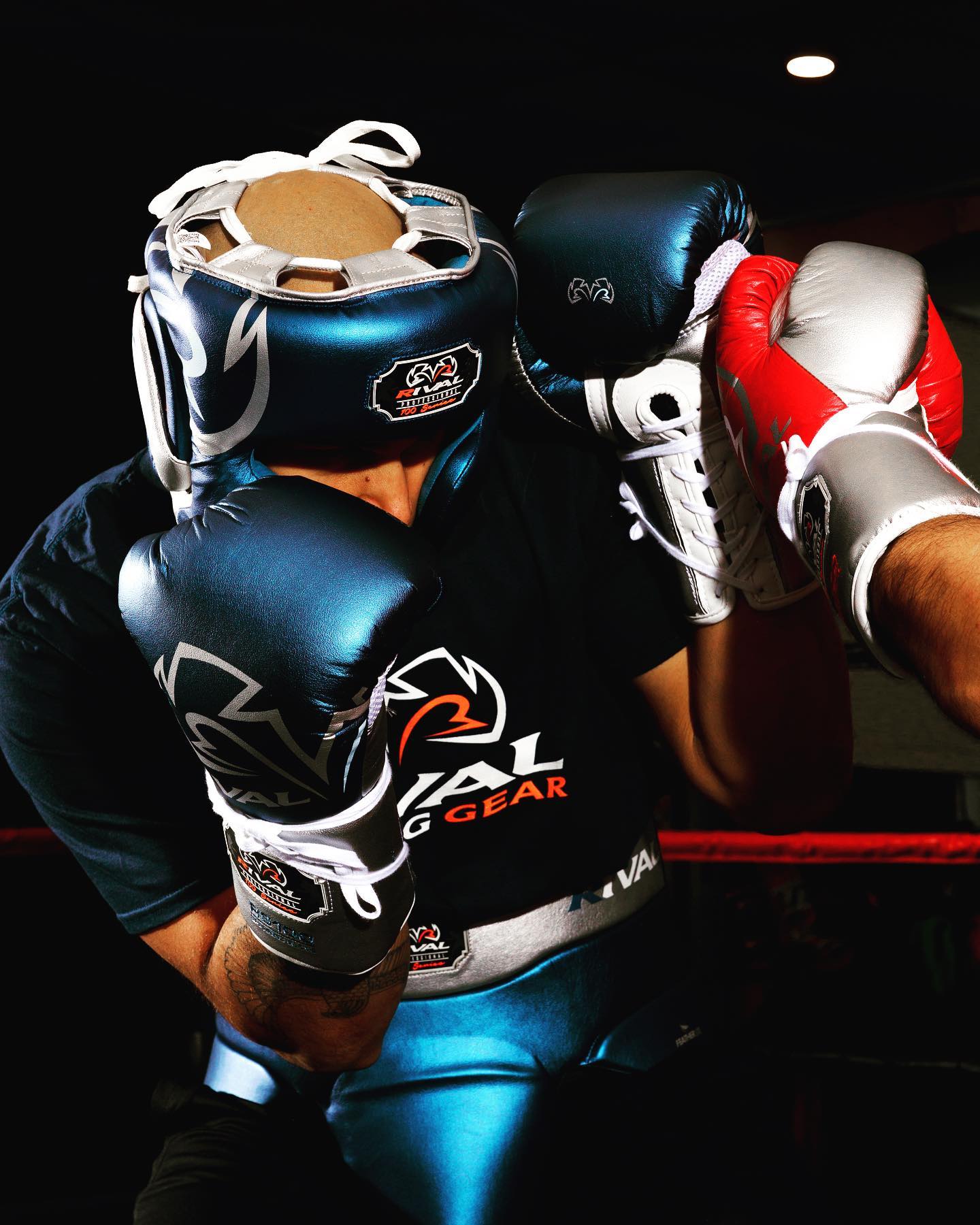 Person wearing boxing gear with a focus on gloves and headgear, set against a dark background.
