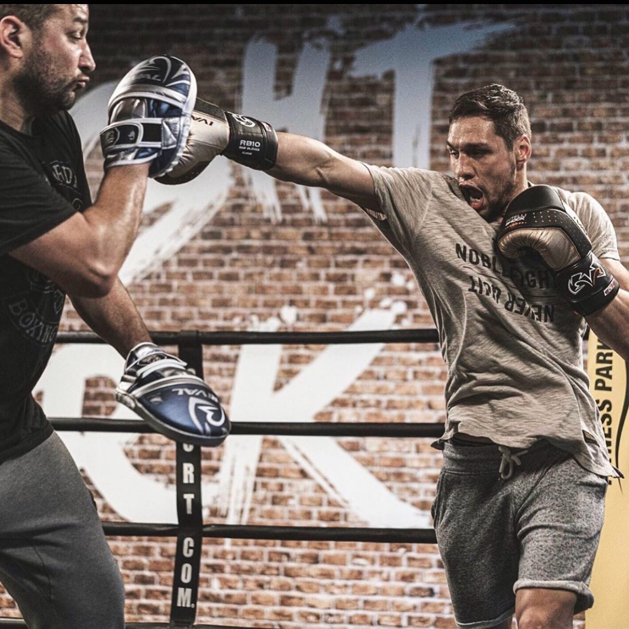 Two boxers in a boxing ring with a brick wall background