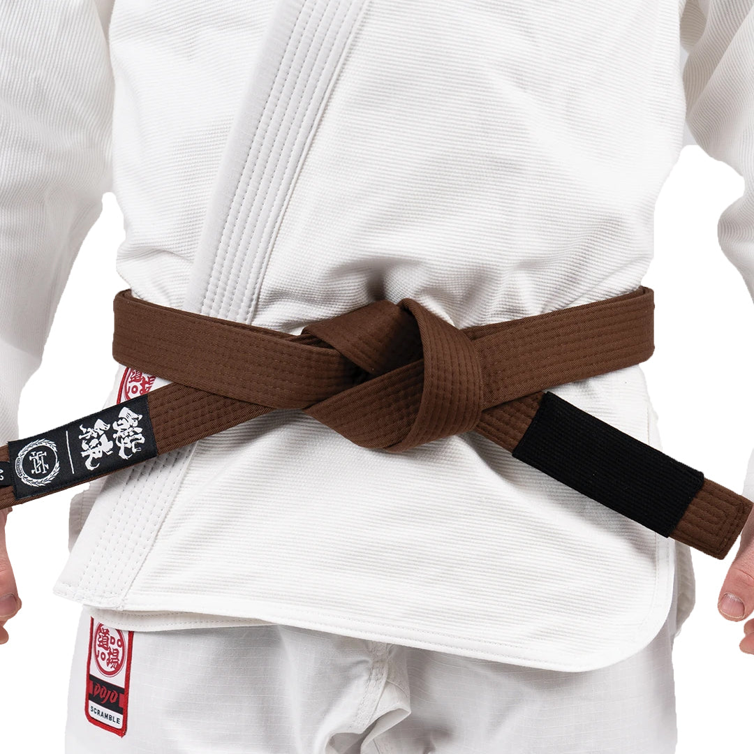 Person wearing a white martial arts uniform with a brown belt and visible brand logo.