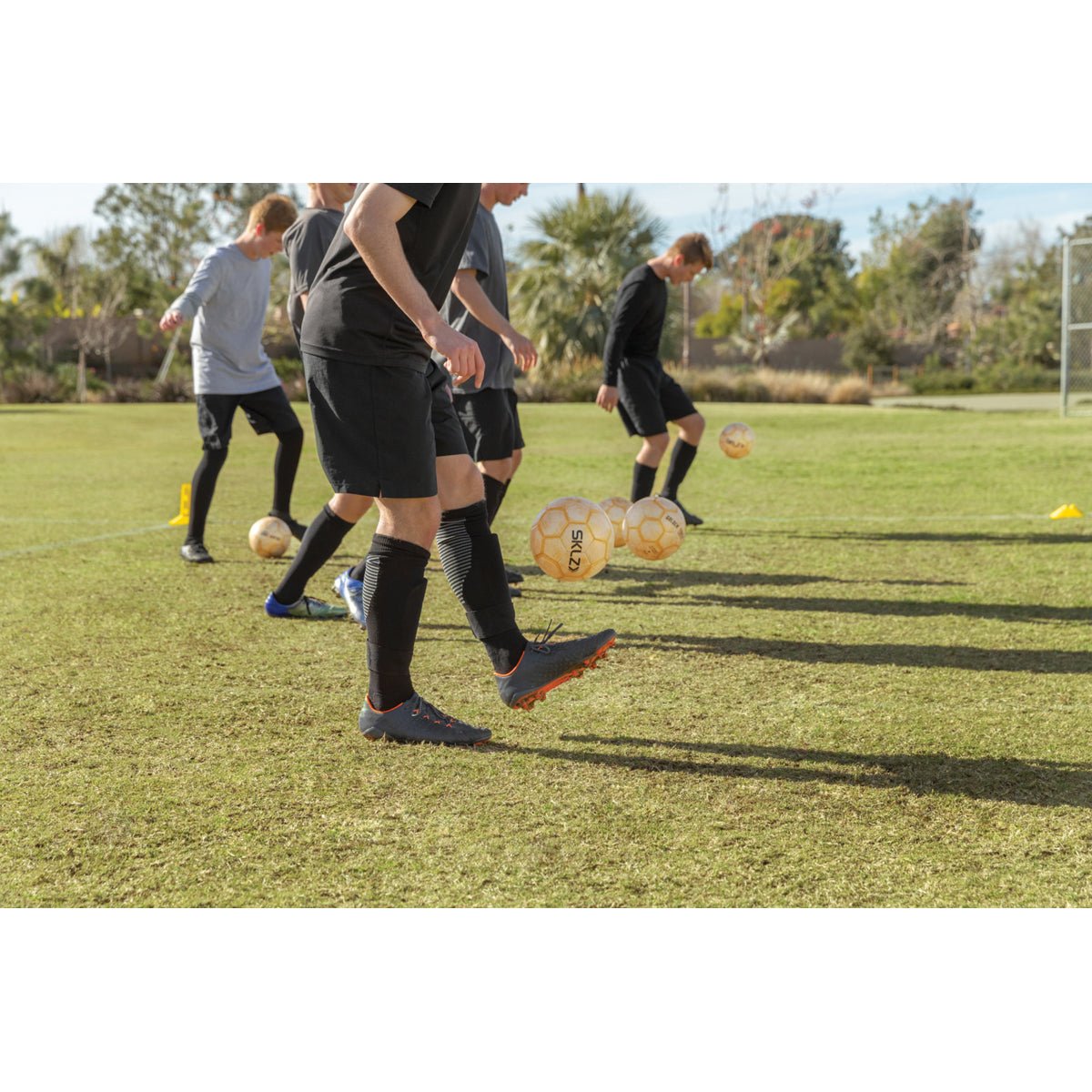People playing soccer on a grass field with multiple weighted soccer ball in the air.