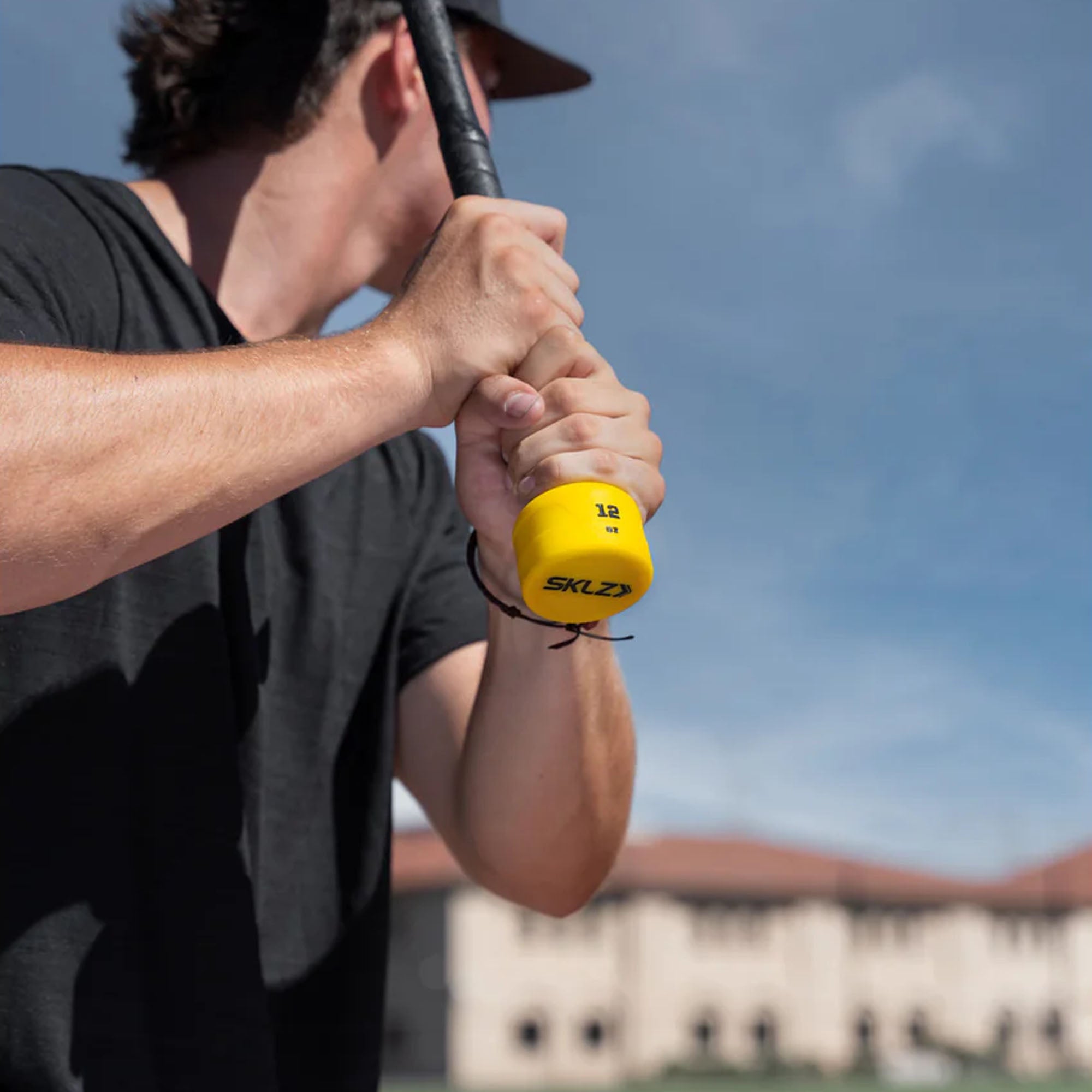 Person holding a yellow SKLZ handle weighted swing knob training aid against a blurred outdoor background