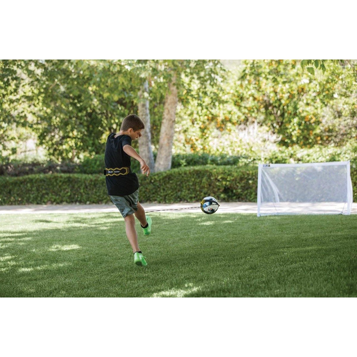 Child playing solo soccer trainer in a grassy area with a goalpost.