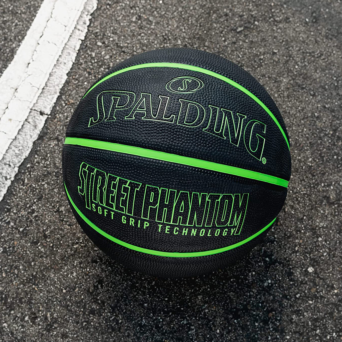 Black basketball with green text on a street surface, featuring Spalding branding.