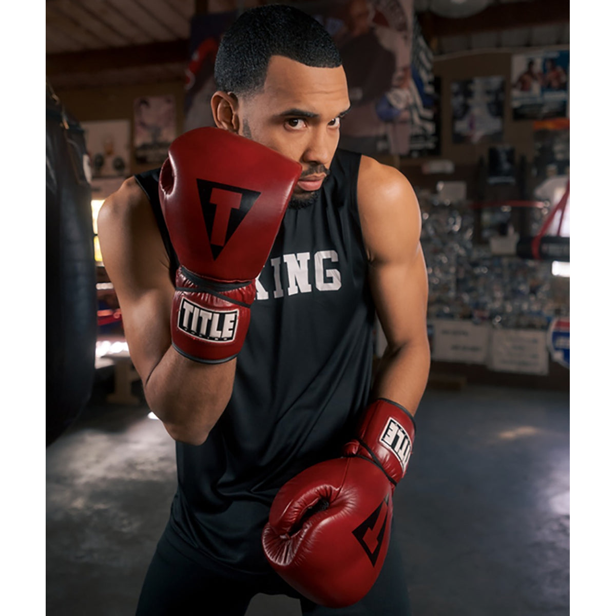 Man wearing red boxing gloves and a black tank top with 'King' printed on it, in a boxing ring.
