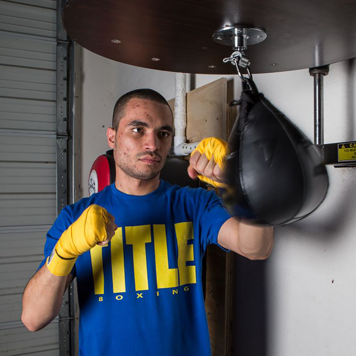 Man in blue TITLE Boxing shirt and yellow Title Boxing Leather Speed Bag