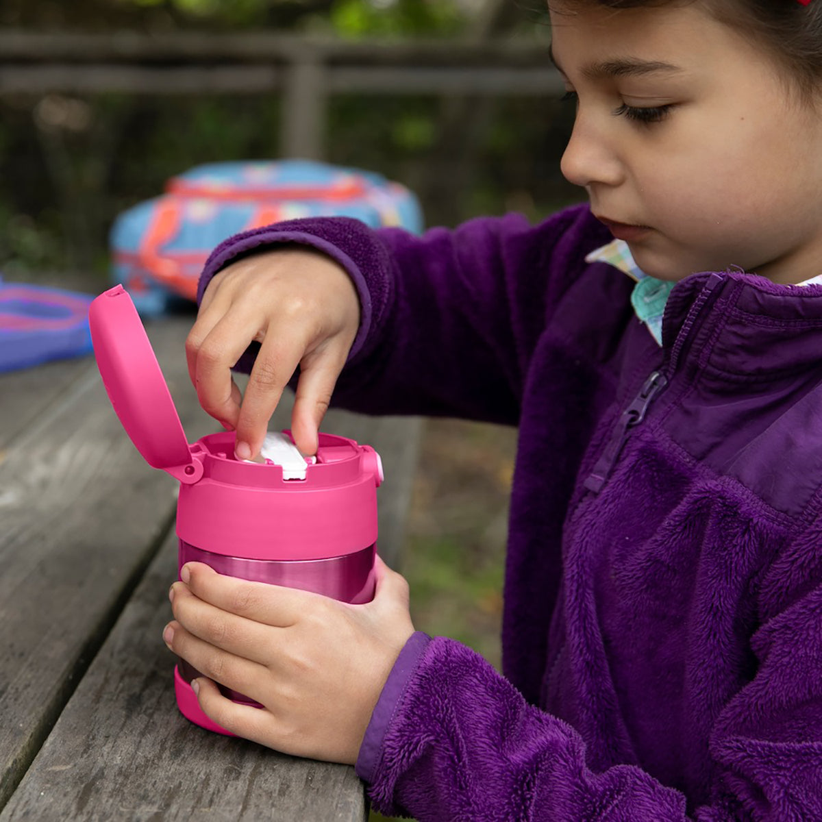 Child in purple jacket interacting with a pink container outdoors - Forza Sports