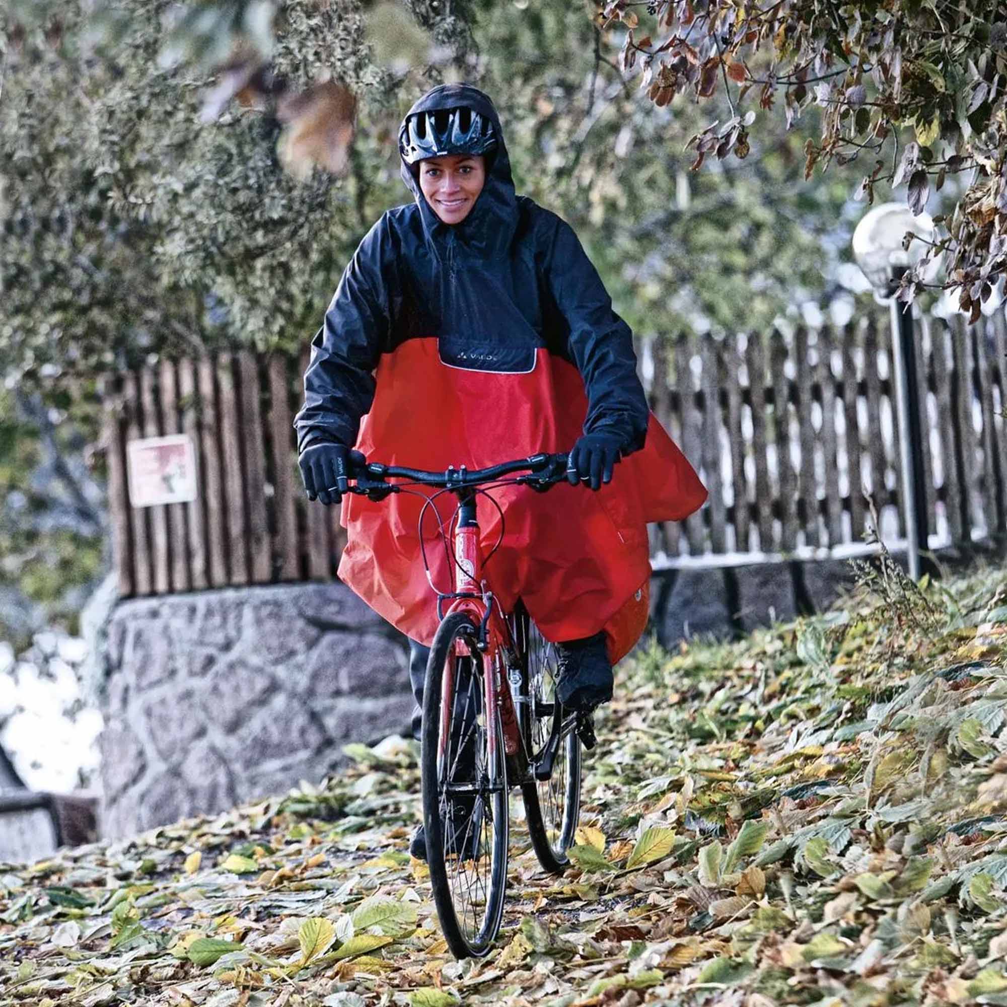 Person riding a bicycle wearing red biking rain poncho pants and a black jacket in a forested area.