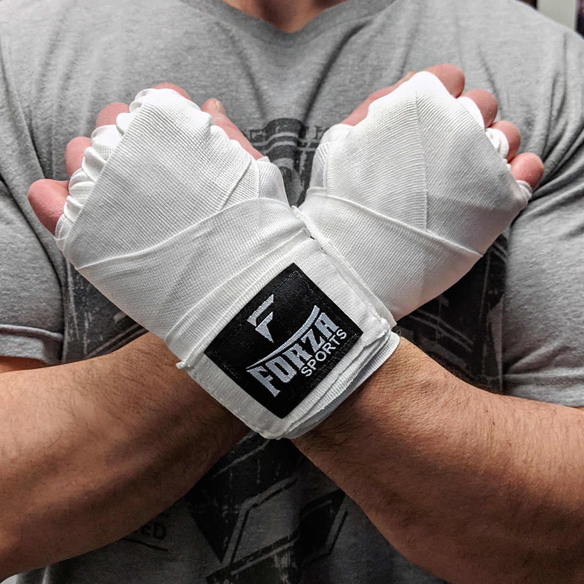 Person wearing white boxing hand wraps with Forza Sports logo on a gray shirt background