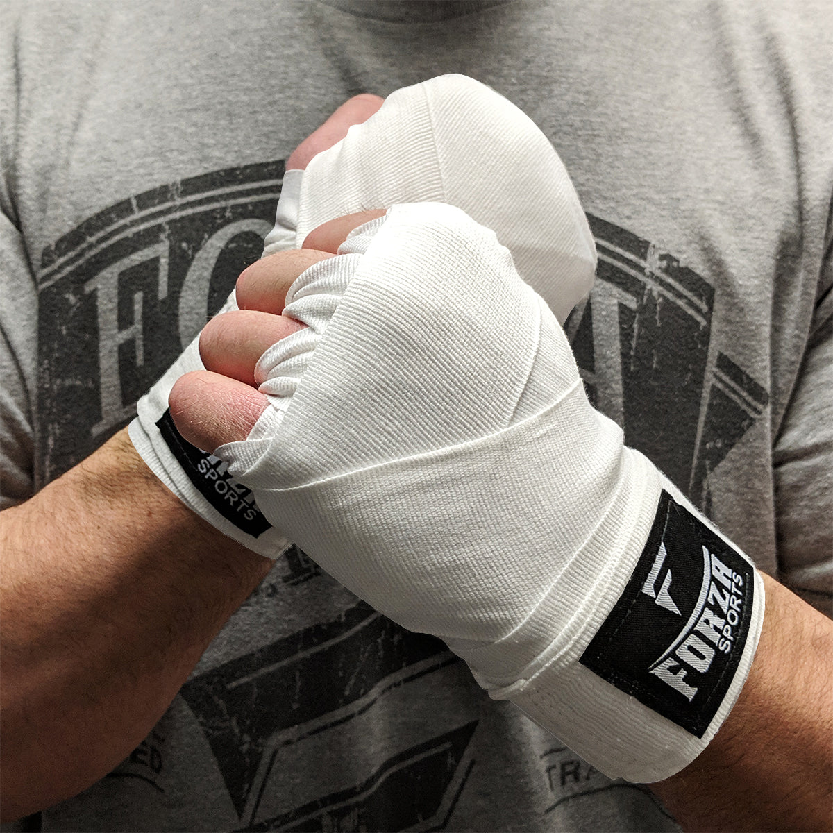 Person wearing white boxing hand wraps with FCS logo, against a gray t-shirt background