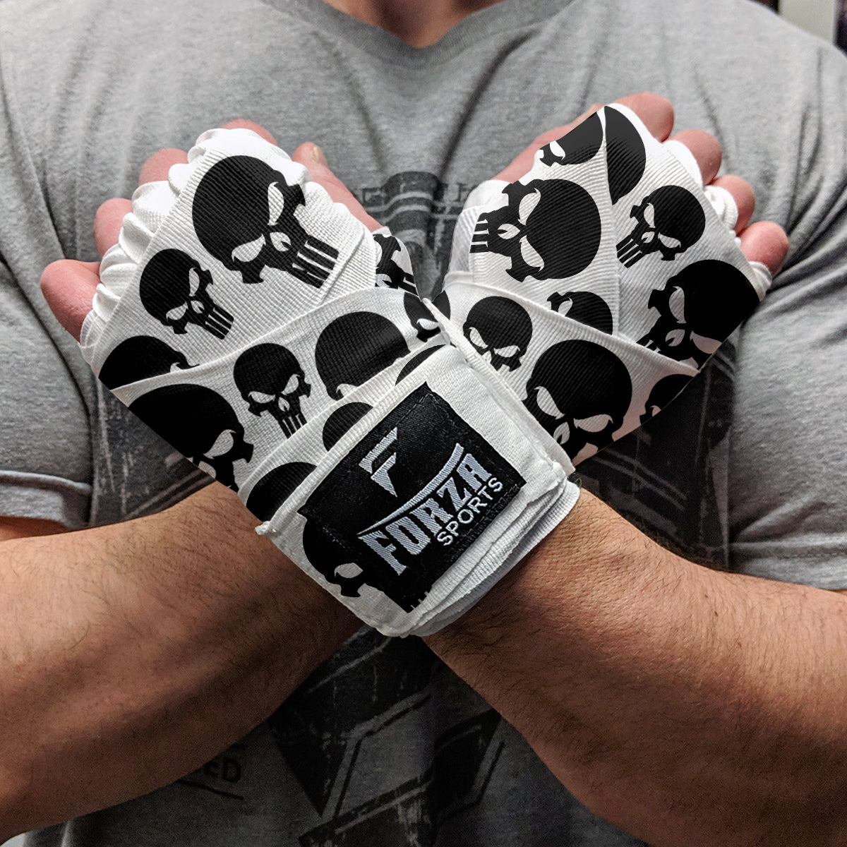 White boxing gloves with black skull patterns held by a person wearing a gray shirt.