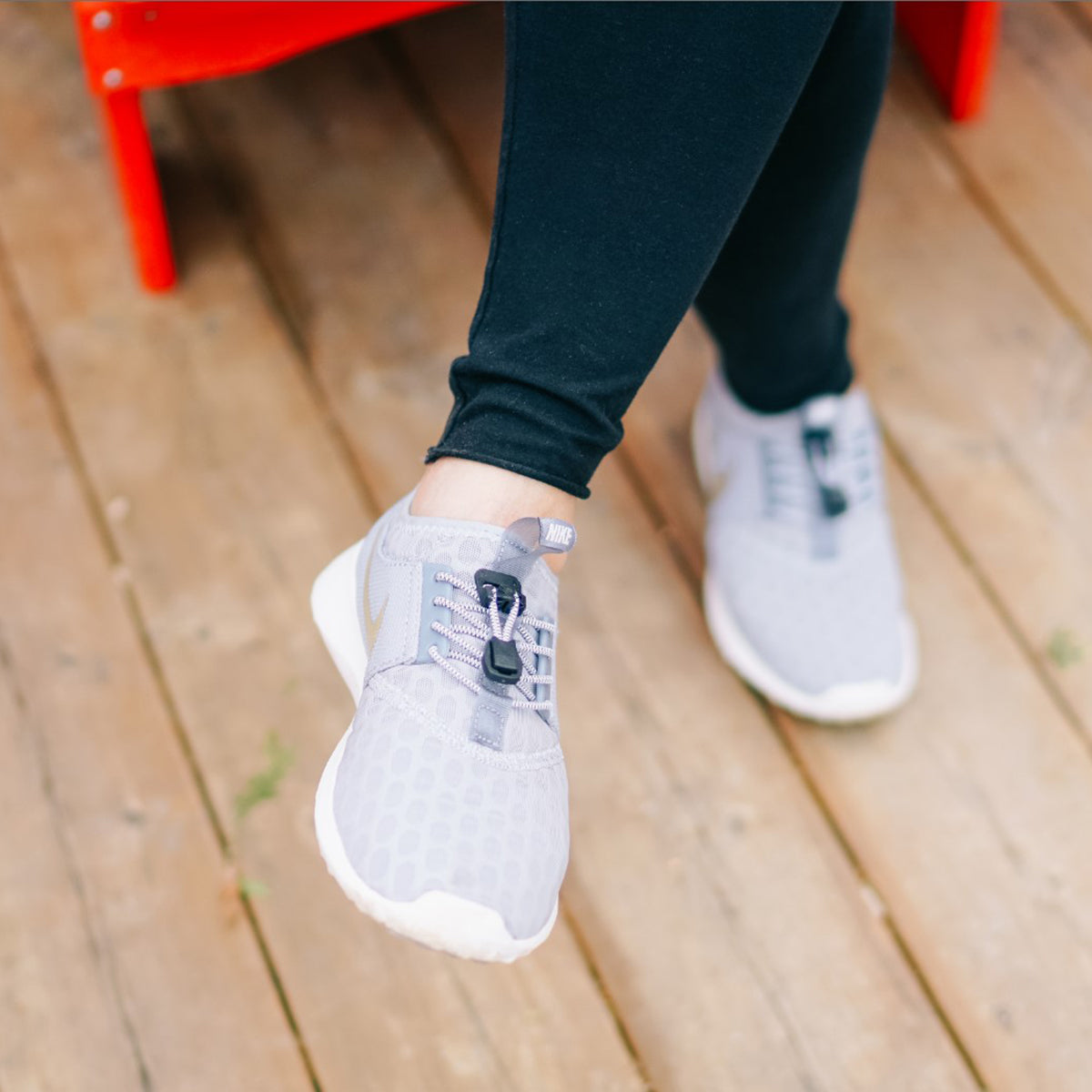 Person wearing gray sneakers on a wooden floor with a red chair in the background - Forza Sports