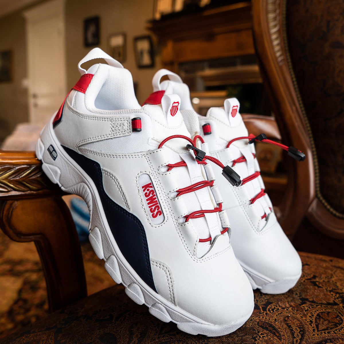 White sneakers with red laces and black accents on a wooden surface - Forza Sports