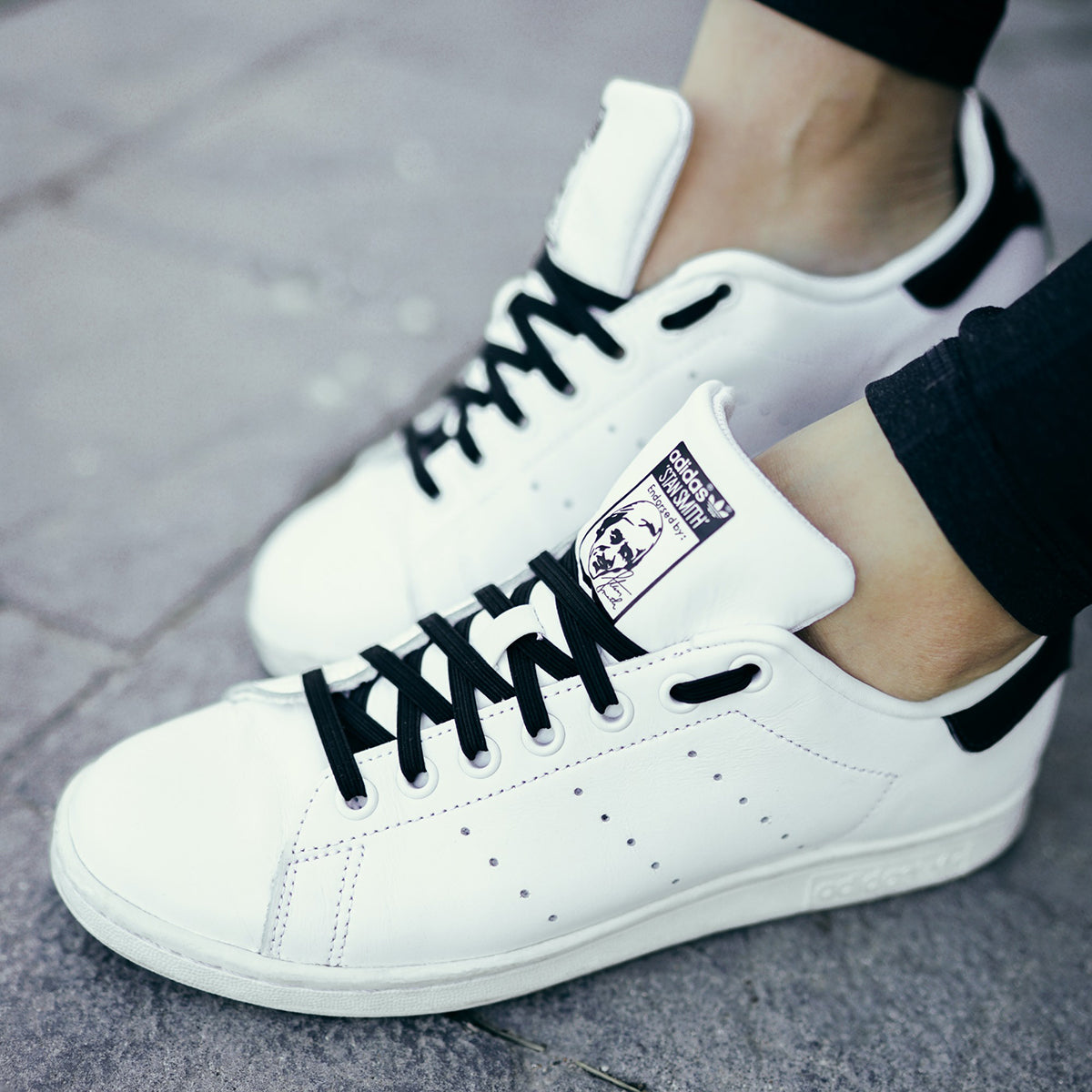White sneakers with black laces worn on a gray pavement