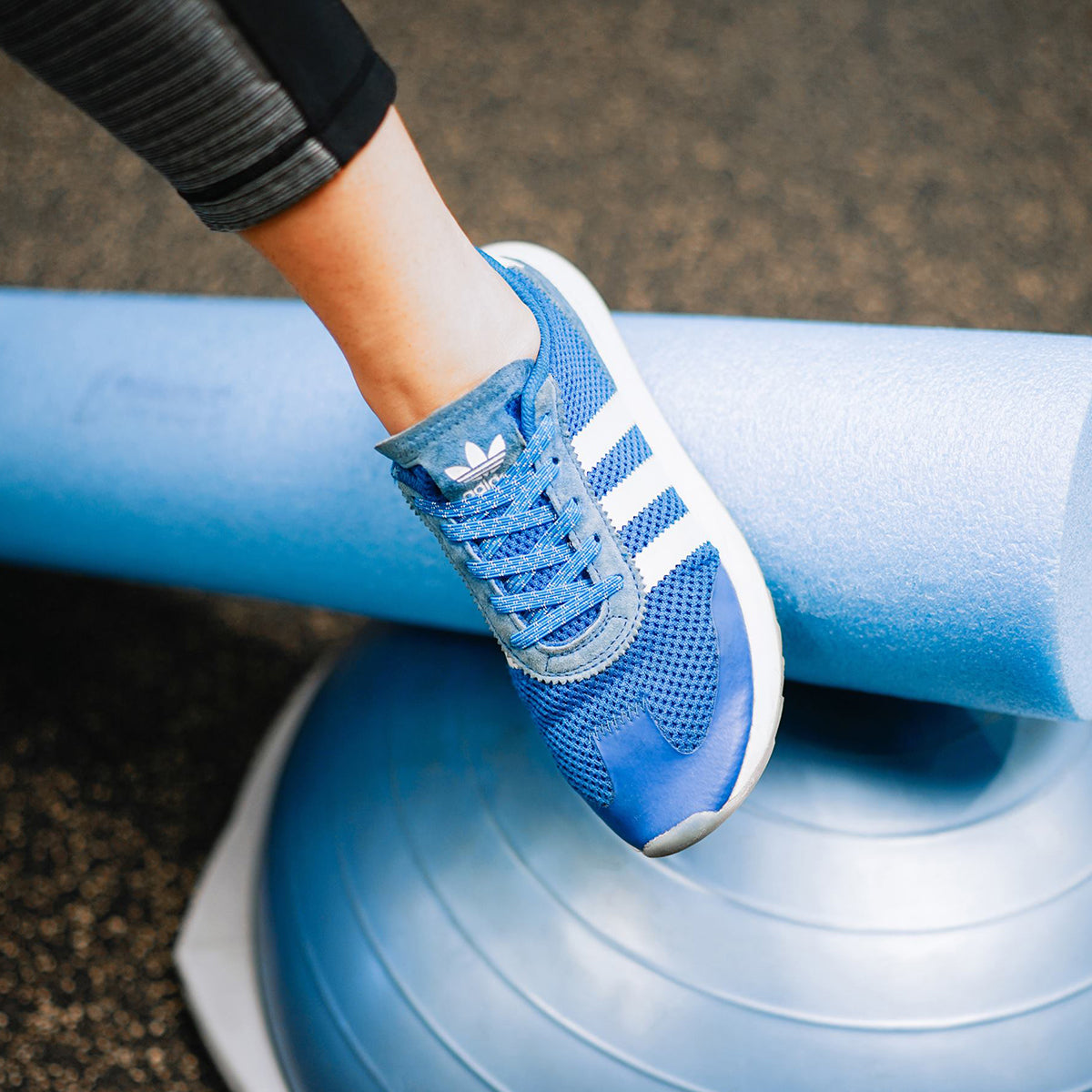 Person wearing blue Adidas sneakers on a blue exercise ball