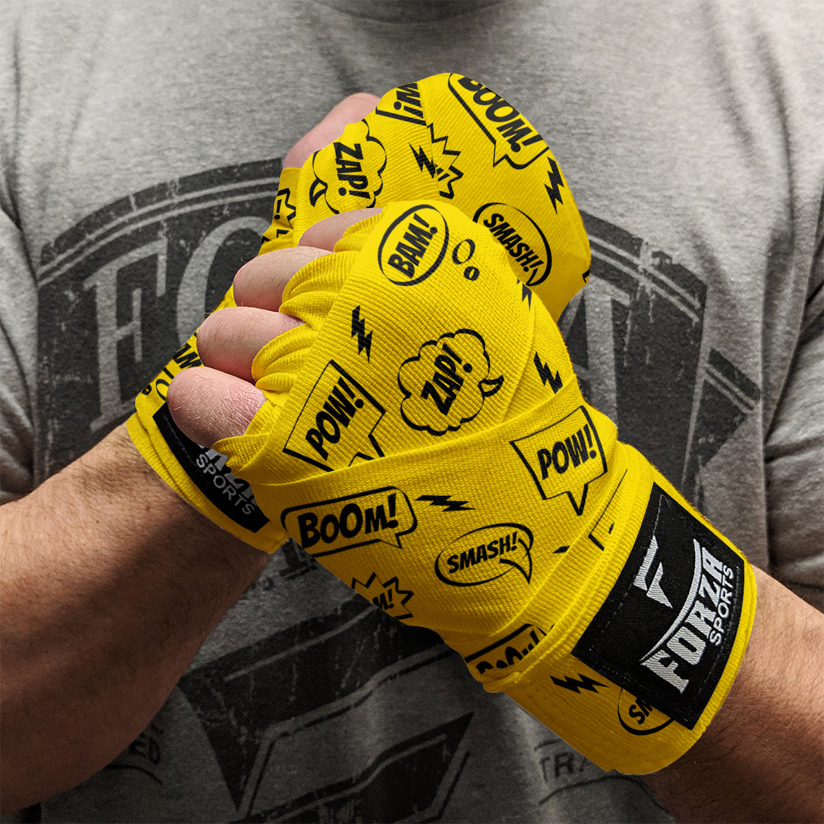 Comic Book Yellow boxing hand wraps with black text and logos, worn by a person against a gray t-shirt background.