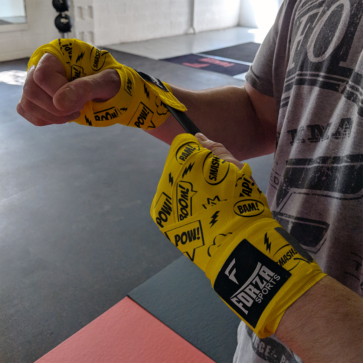 Person wearing yellow boxing hand wraps with black text and 'Furzer Sports' branding in a gym setting.