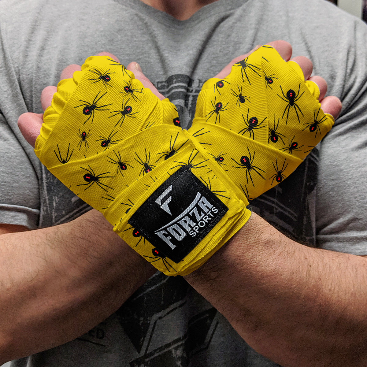 Yellow wrist wraps with black spider pattern and Forza Sports logo being worn by a person.