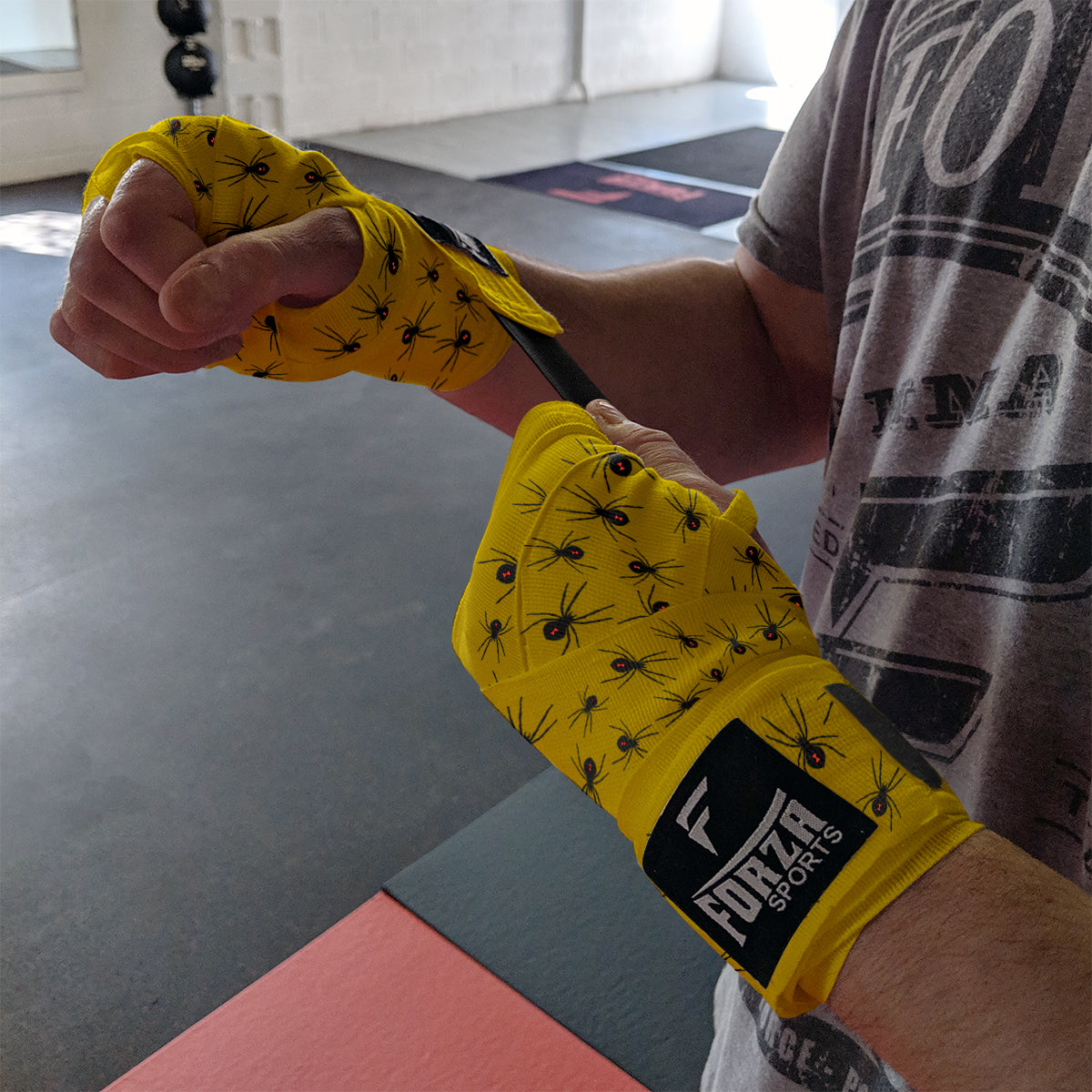 Person wearing yellow boxing gloves with black patterns, wrapped around their hands, in a gym setting.