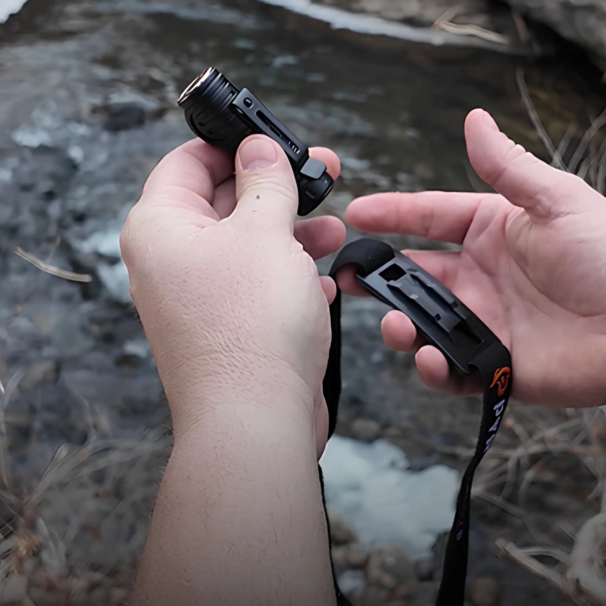 Person holding a small black flashlight with a lanyard against a natural background.